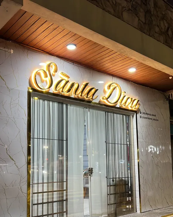 Fachada da Santa Diva à noite: mármore branco, letreiro dourado aceso e forro de madeira